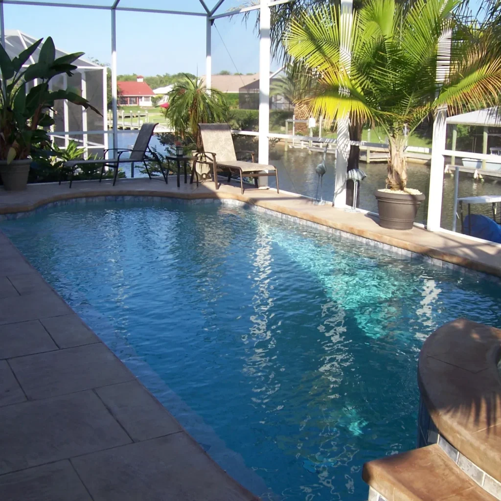 A screened freeform pool with a stamped concrete deck overlooking a canal with a dock.