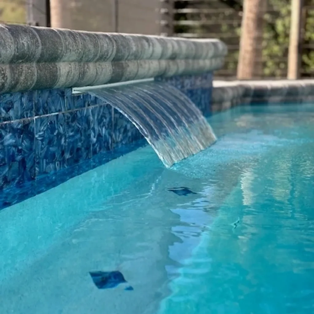 Close-up of a sheer descent waterfall spilling over a blue tiled wall into a pool.