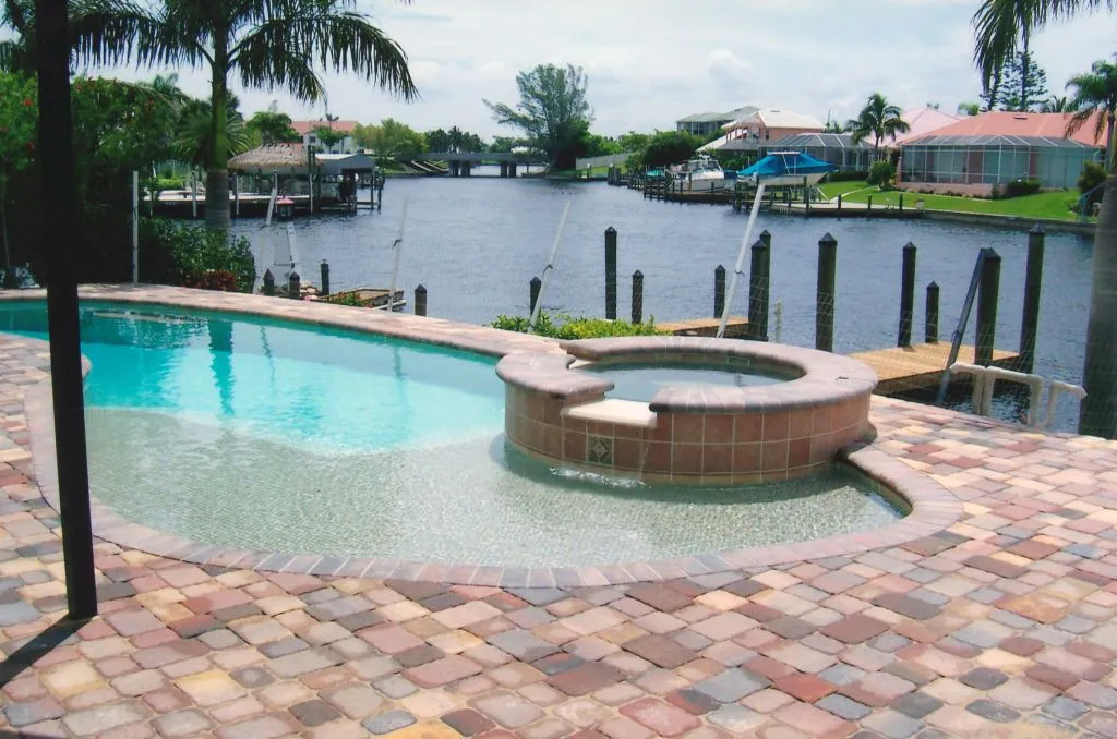 Freeform pool with raised spillover spa on a canal with paver deck and dock.