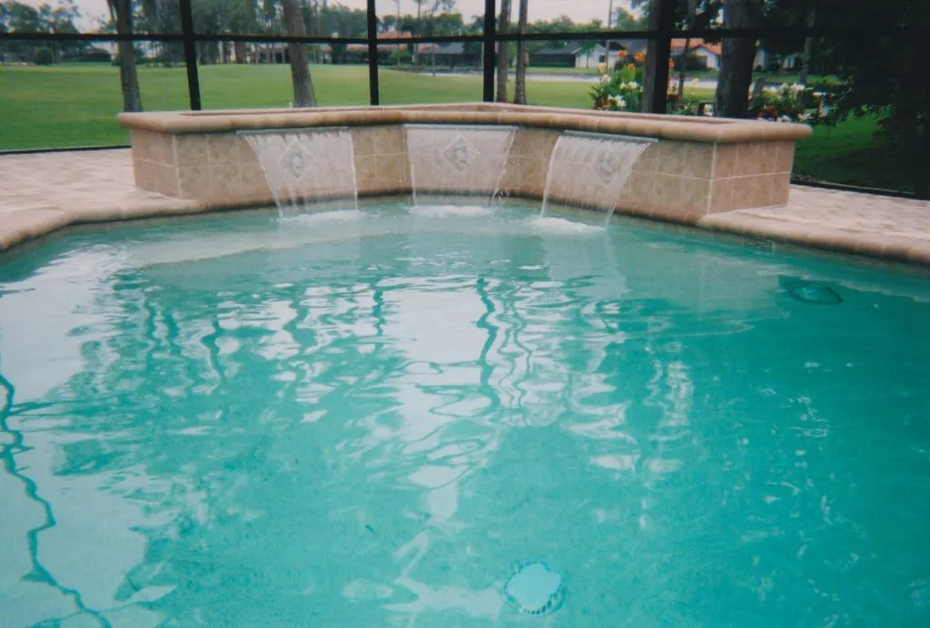 A screened freeform pool with a raised tiled wall featuring three cascading water falls.
