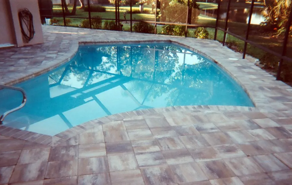 A freeform pool with paver decking under a screened enclosure, backing onto a canal.