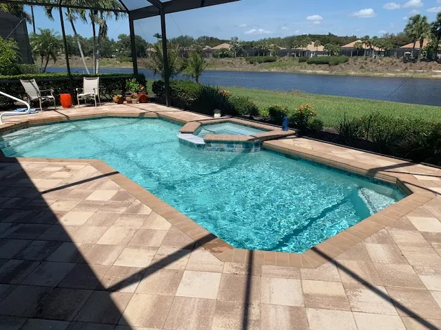 A screened pool with an attached spa overlooks a lake and community landscape.