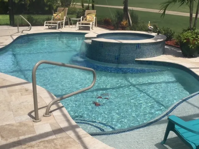 A freeform pool with a raised spa spilling into it, travertine deck, and a golf course visible beyond the screen enclosure.
