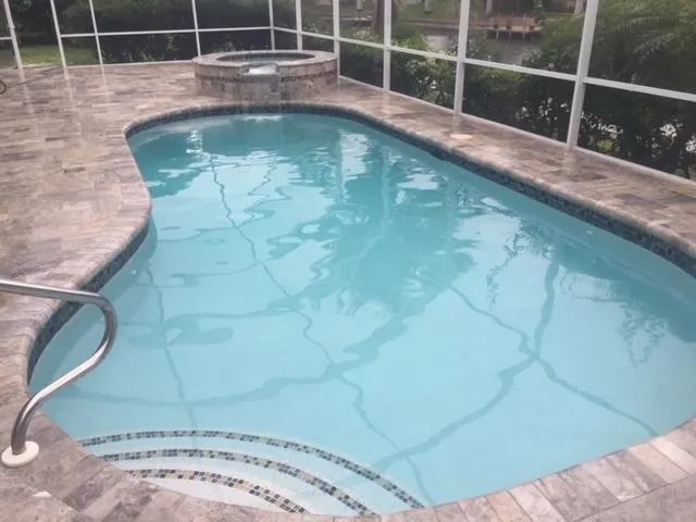 A freeform pool with a raised spa on a screened lanai overlooking a canal.