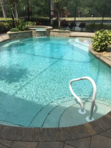 A freeform pool with a raised spillover spa and screened lanai overlooking a pond and golf course.