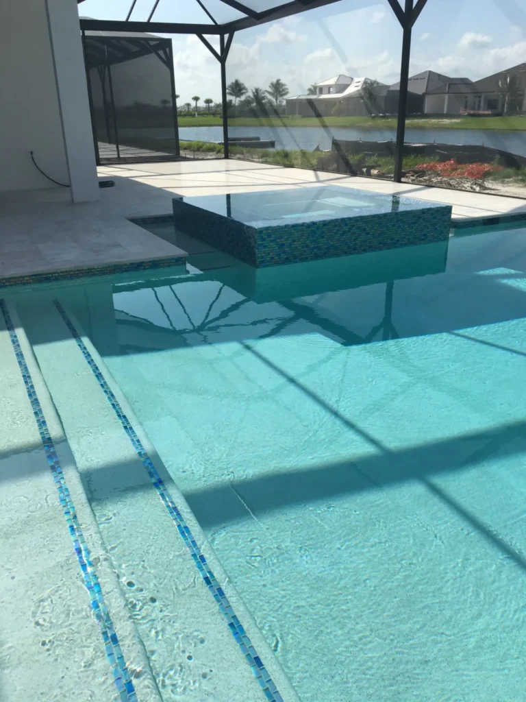 A rectangular pool with a raised glass-tile spa and blue mosaic steps under a screened enclosure overlooking a lake.