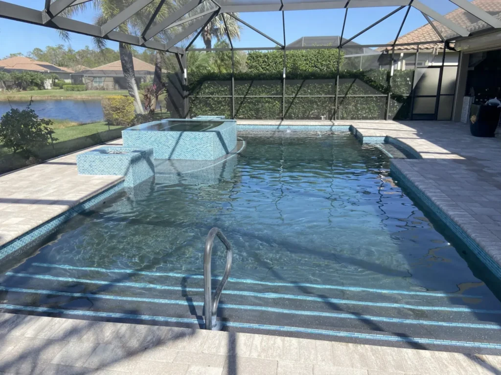 A rectangular pool with a raised tiled spa under a screened lanai overlooking a pond.
