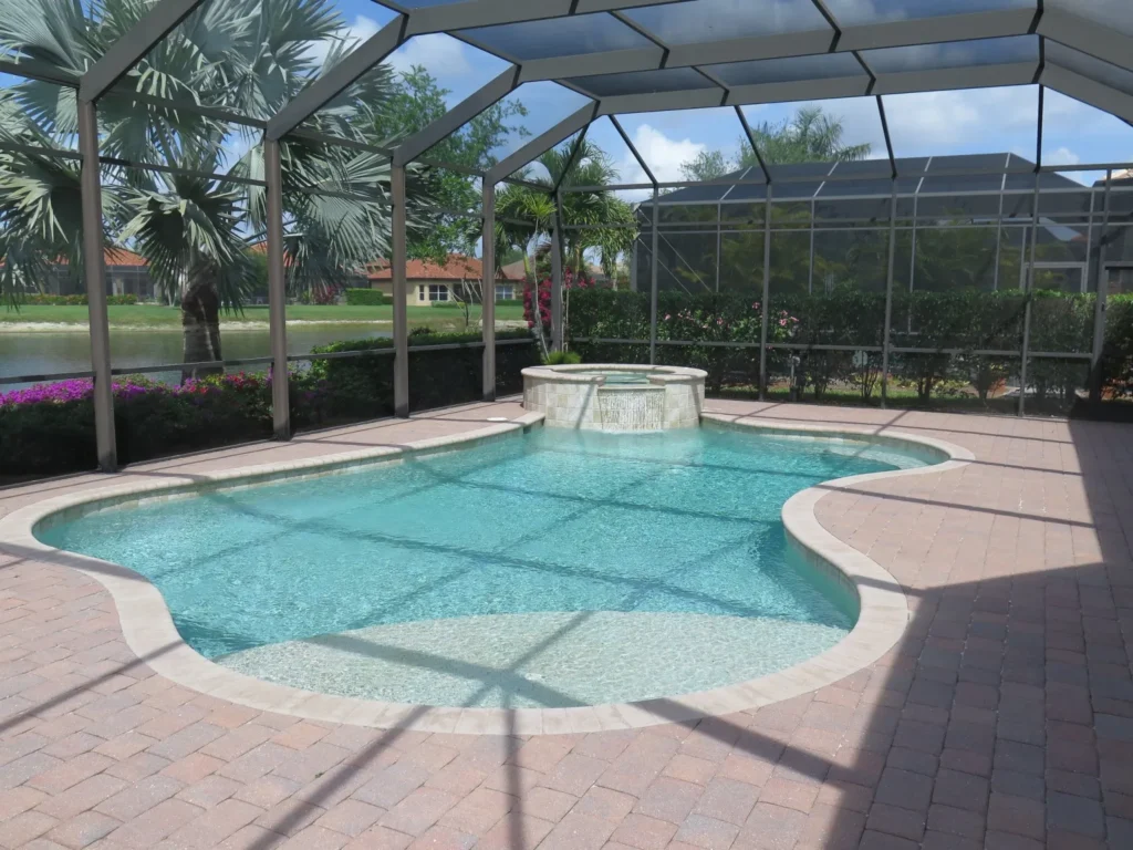 Freeform pool with raised stone spa spilling into the water under a screened lanai overlooking a canal.
