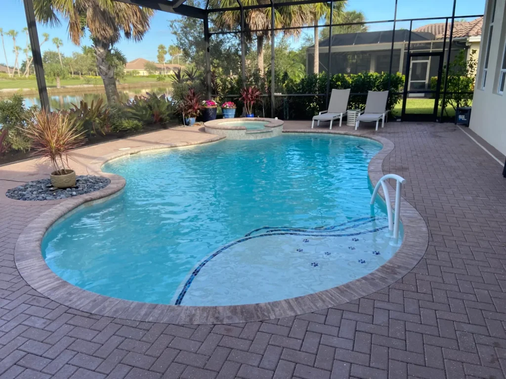 A freeform pool with a raised spa and paw-print tanning ledge tiles inside a screened lanai overlooking a pond.