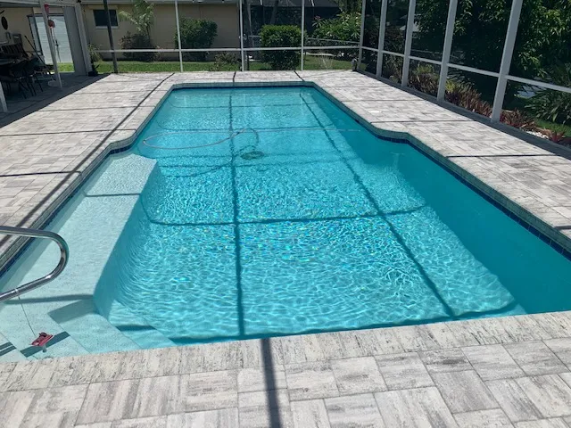 A rectangular pool with a shallow tanning ledge under a screened lanai enclosure.