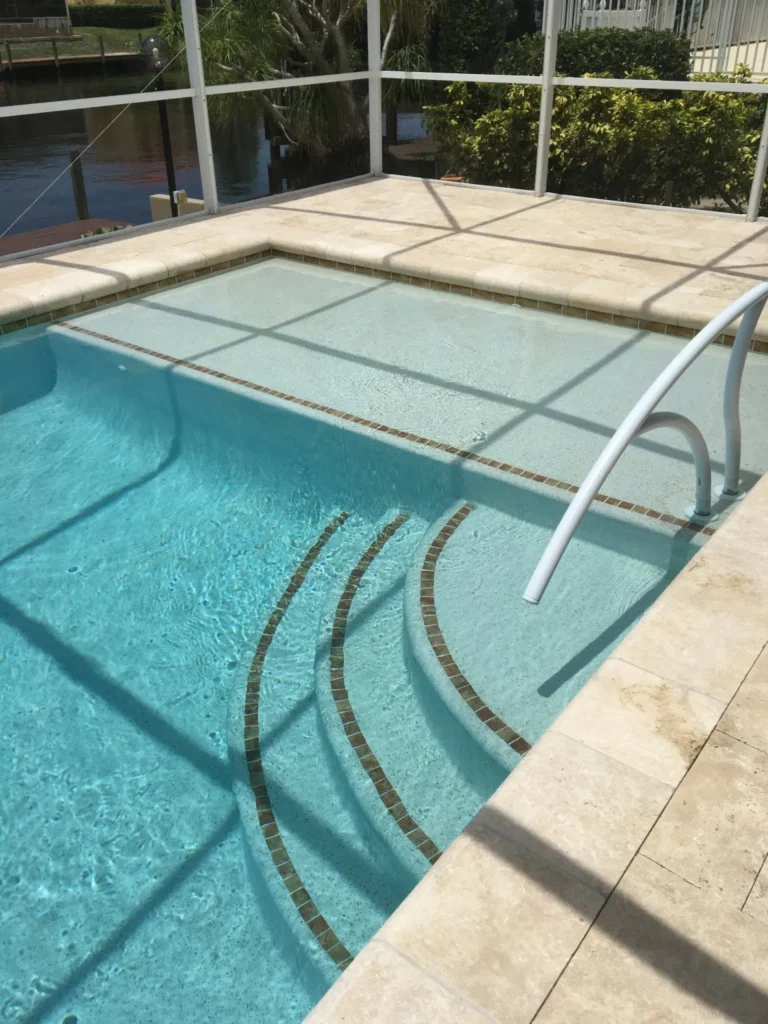 Close view of pool entry steps and tanning ledge with tile accents, canal visible beyond the screen enclosure.