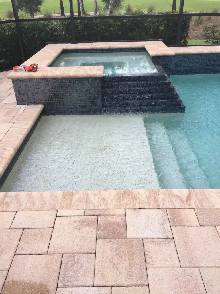 A raised glass-tile spa spills water down steps into a pool under a screened lanai.