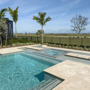 A modern rectangular pool with an integrated raised spa and travertine deck overlooking an open field.