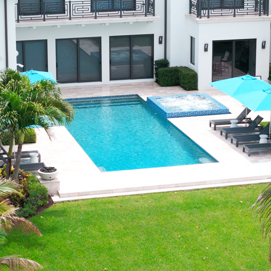 Rectangular pool with an attached raised spa on a stone patio behind a large modern home.