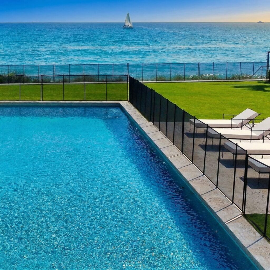 Pool edge with safety fence overlooking the ocean and a sailboat.