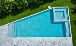Aerial view of an angular geometric pool with an attached raised-look square spa and tiled tanning ledge steps, surrounded by travertine decking and lawn.