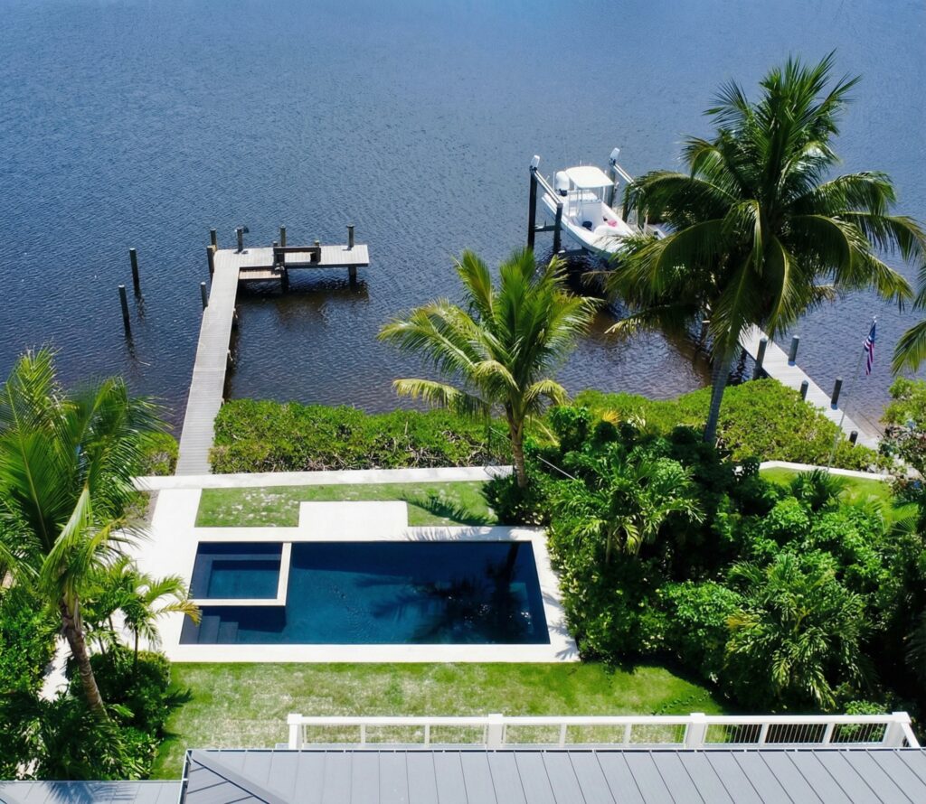 Aerial view of a small rectangular pool with dark plaster finish set in a lawn beside a canal with a private dock.