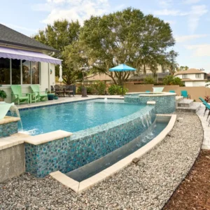 A raised infinity-edge pool with glass tile spa and cascading water bowls in a landscaped backyard.