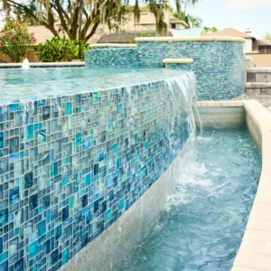 A vanishing-edge pool wall covered in blue mosaic tile spills water into a lower catch basin.