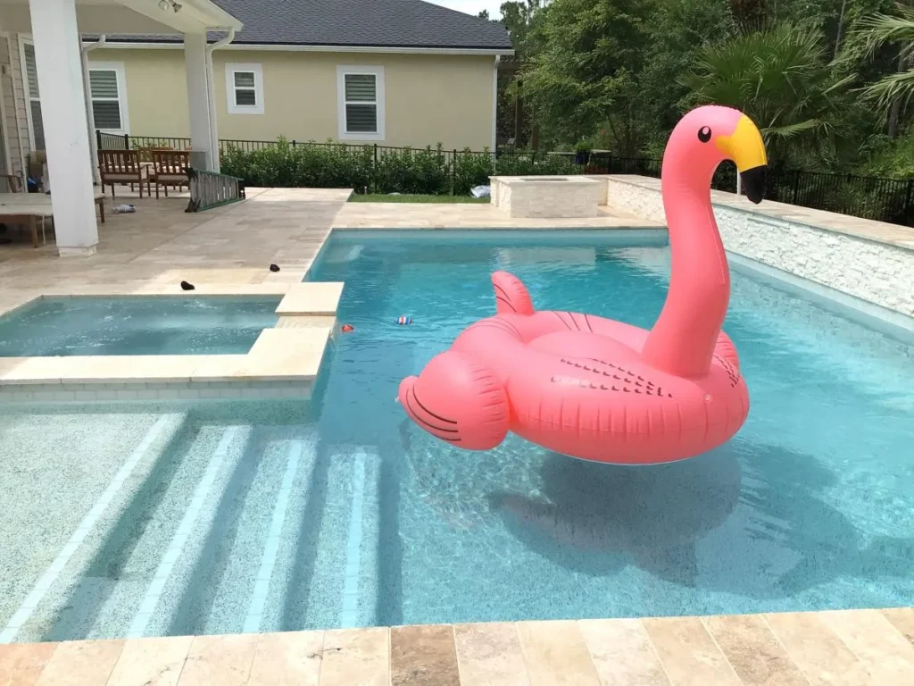 A rectangular backyard pool with a raised spa and a large inflatable flamingo float.