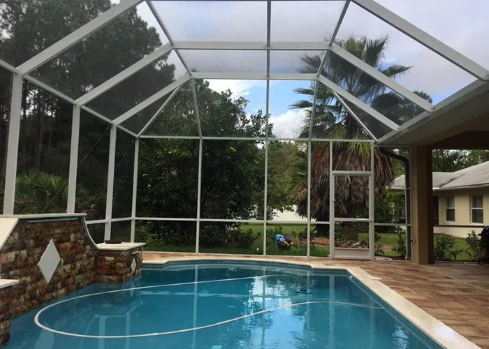 A small freeform pool with a stone waterfall feature under a screened patio enclosure.