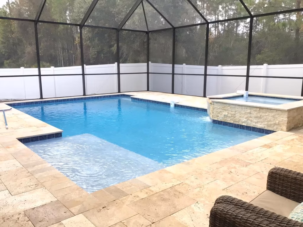 A rectangular pool with a sun shelf and raised stone spa inside a screened enclosure.