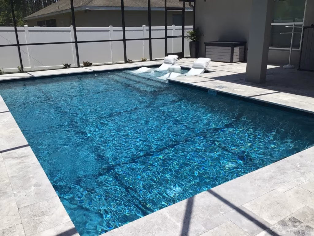 A rectangular pool with a shallow sun shelf and two loungers under a screened lanai.