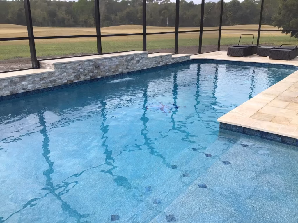 A screened rectangular pool with a stacked stone waterfall wall overlooking a golf course fairway.