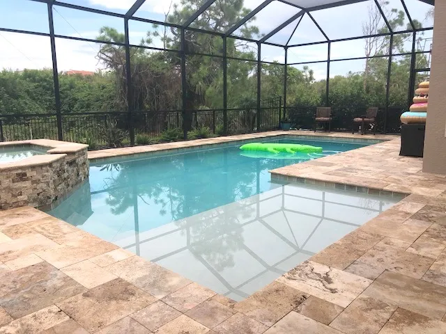 A screened lanai with a small L-shaped pool, raised stone spa, and a floating inflatable toy on the water.
