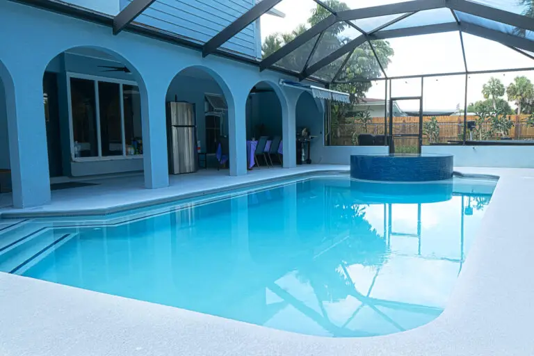 A rectangular pool with a round raised spa under a screened patio enclosure attached to a blue house.