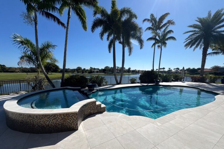 A freeform pool with a raised mosaic-tiled spa overlooks a lake and golf course lined with palm trees.