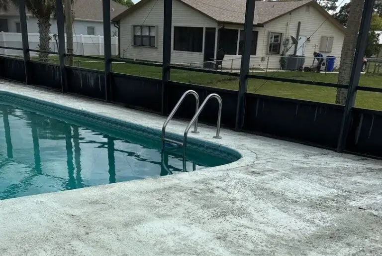 A corner of a screened pool with a stainless steel ladder and worn concrete deck.