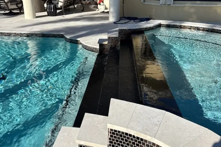 A raised dark-tiled spillway channel connects two sections of a backyard pool under a covered lanai.