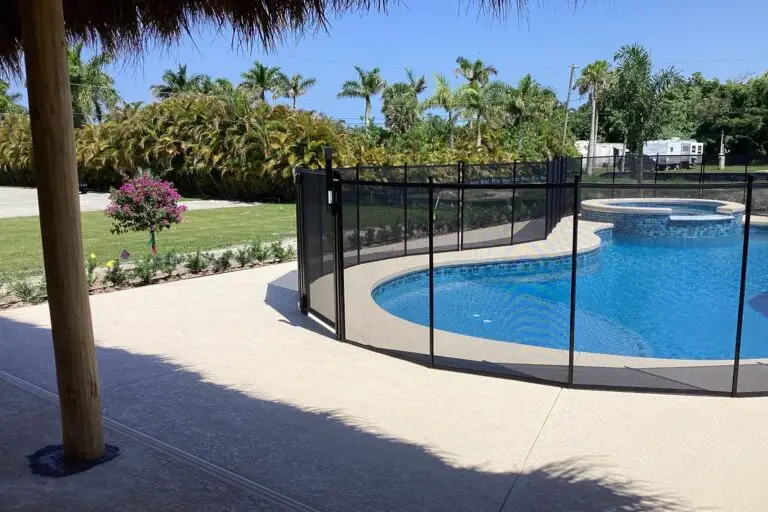 A freeform pool with a raised spa surrounded by a black child-safety fence and palm trees.