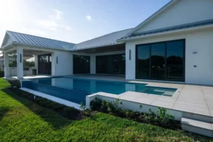 A modern rectangular infinity-edge pool with a raised spa runs along the back of a contemporary home with a metal roof.