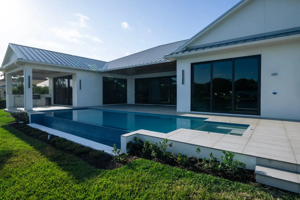 A modern rectangular infinity-edge pool with a raised spa runs along the back of a contemporary home with a metal roof.