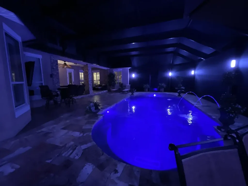 A freeform pool glowing blue with LED lighting at night under a screened lanai.