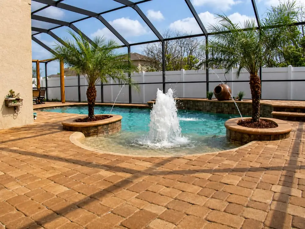 A freeform pool with a central fountain jet and palm-planted islands under a screened enclosure.