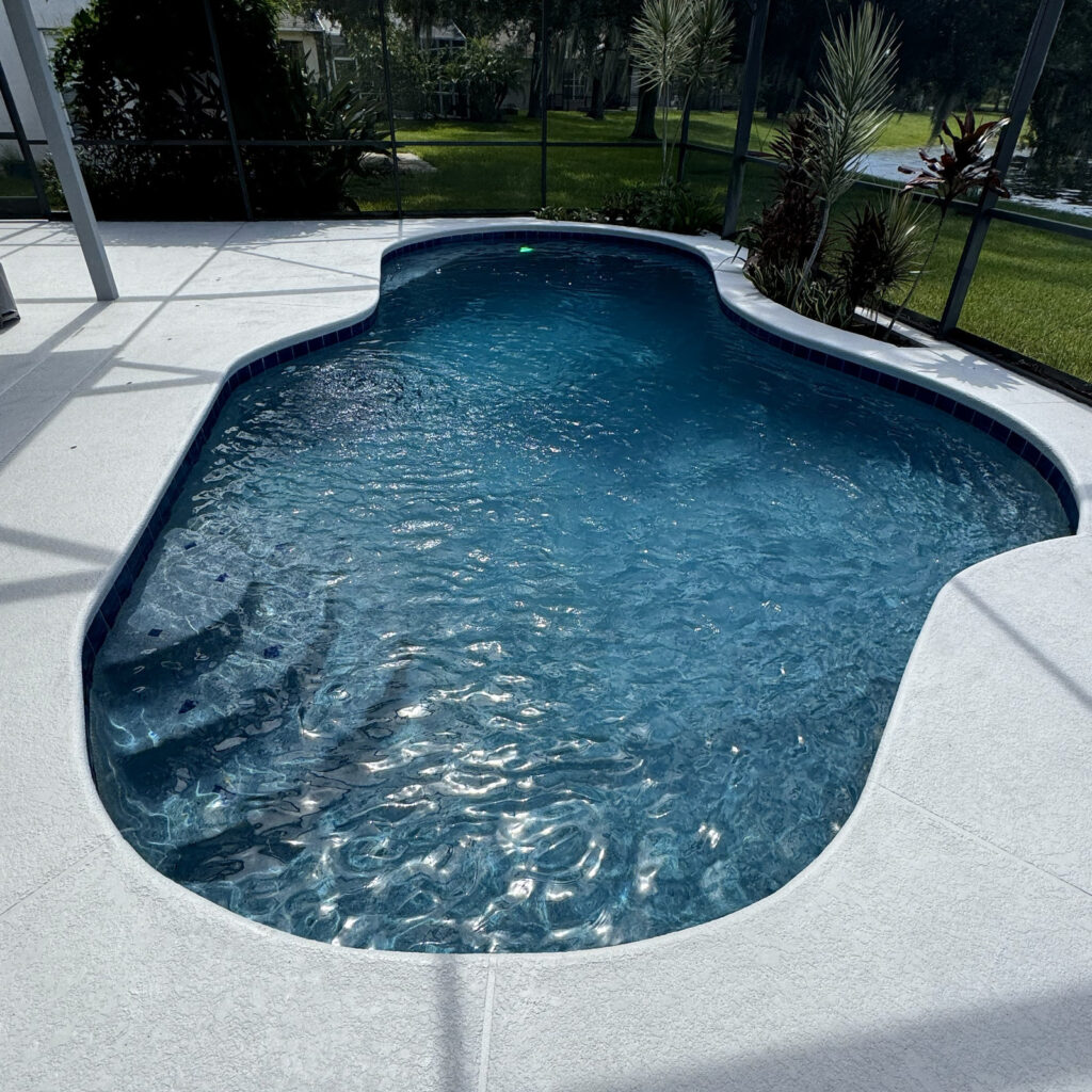 A dark-plastered freeform pool with steps sits under a screened lanai with a canal visible beyond.