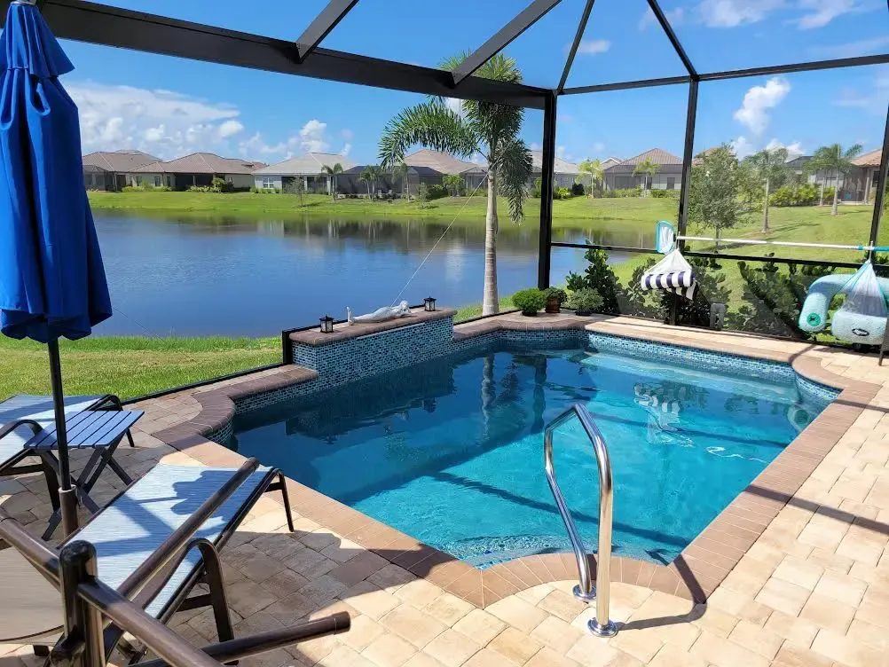 A small geometric pool with a raised tiled wall sits under a screened lanai overlooking a lake.