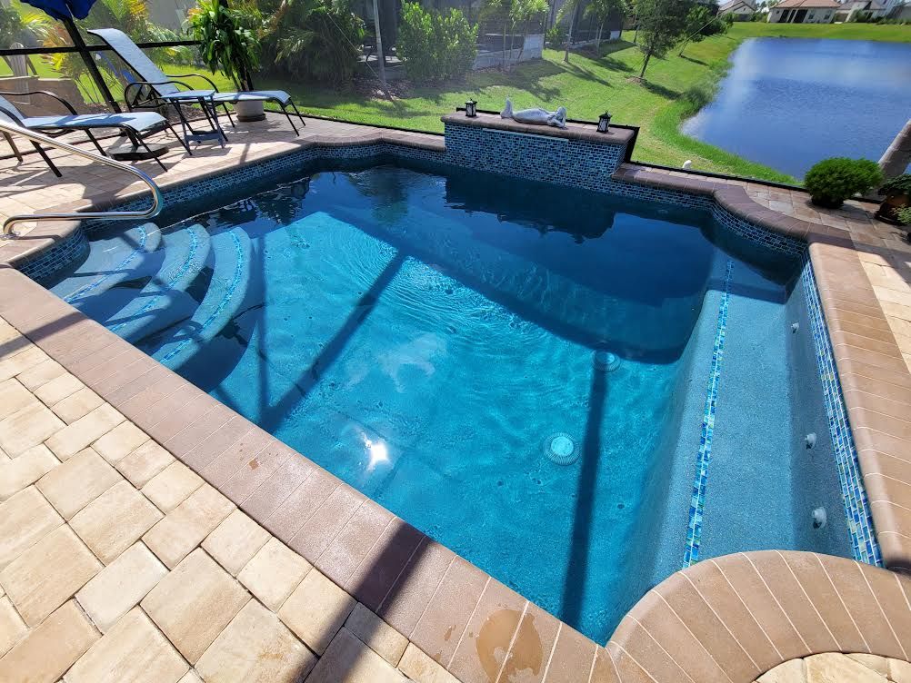 A geometric pool with tiled steps and a raised water feature overlooks a lake, enclosed by a screen cage.