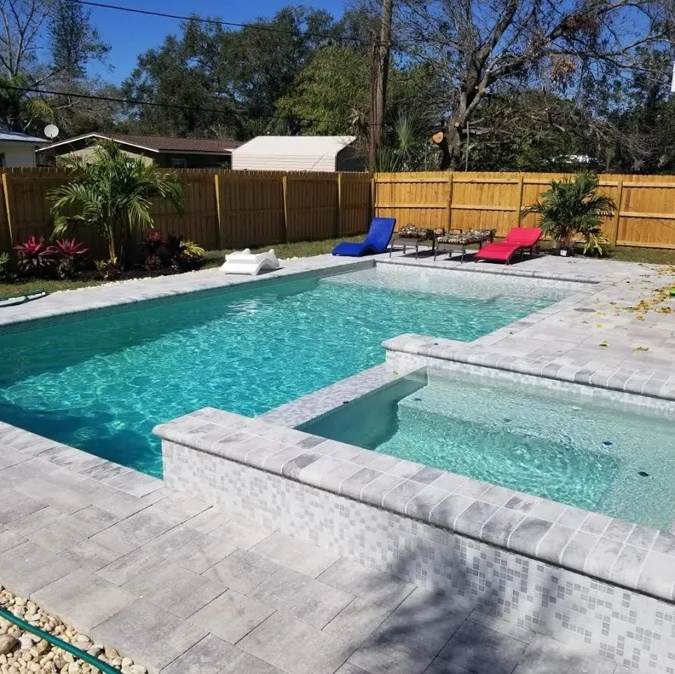 A rectangular backyard pool with an attached raised spa and mosaic-tiled coping on a paver patio.