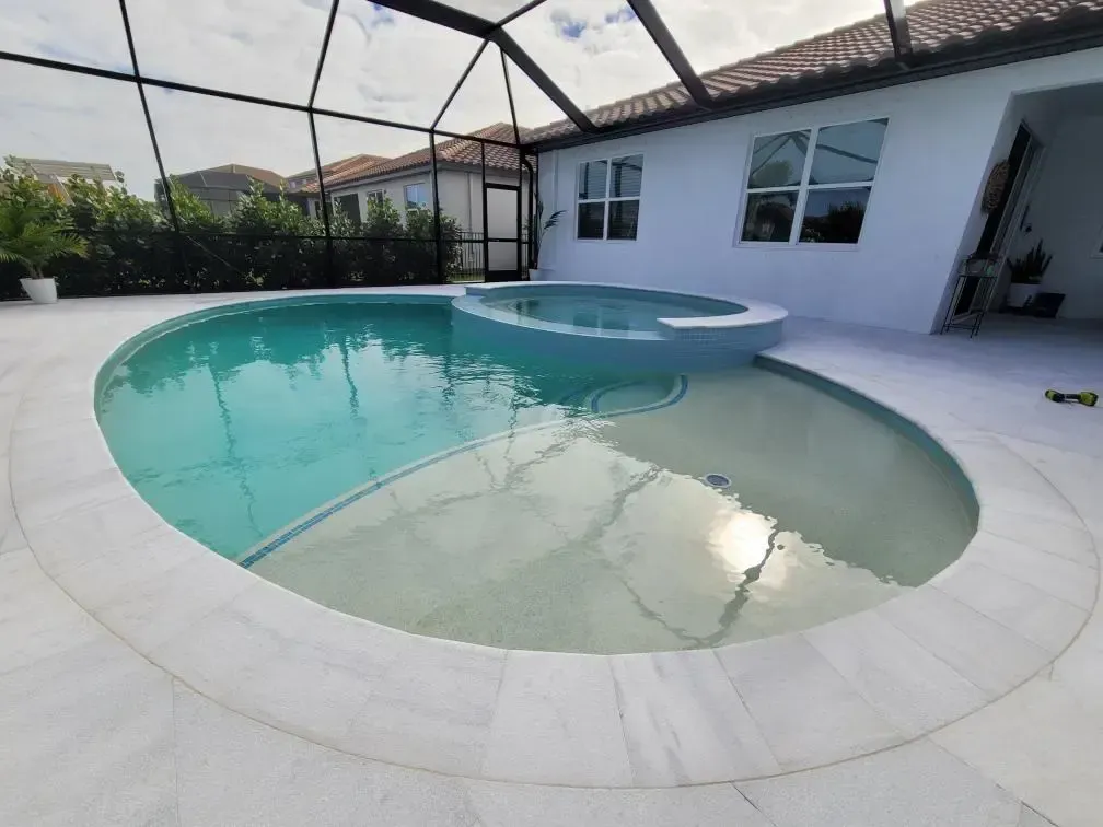 A kidney-shaped pool with a raised spa under a screened lanai, partially filled with water.