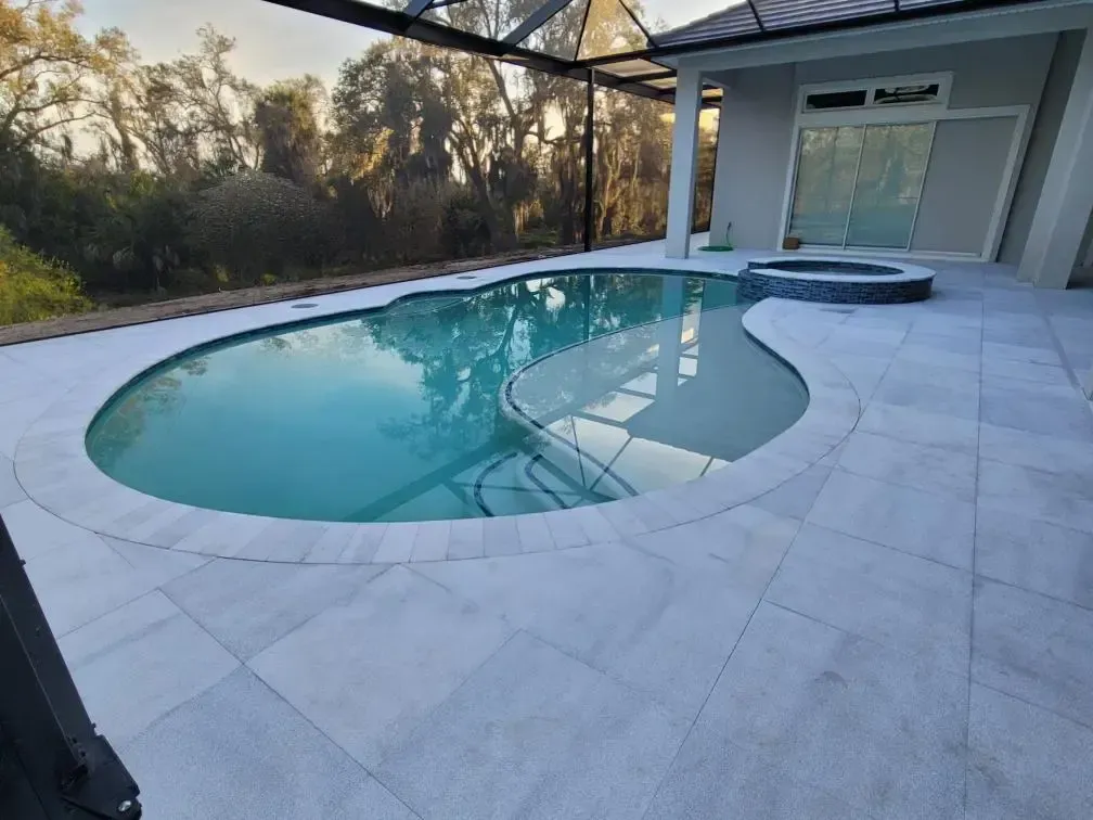 A kidney-shaped pool with a raised spa under a screened enclosure at dusk.