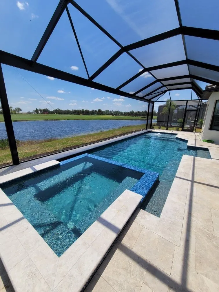 A rectangular pool with an attached spa under a screen enclosure overlooking a pond and golf course.