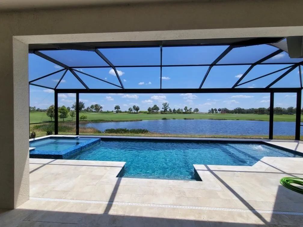 A screened lanai pool with a raised spa overlooks a lake and golf course under a birdcage enclosure.