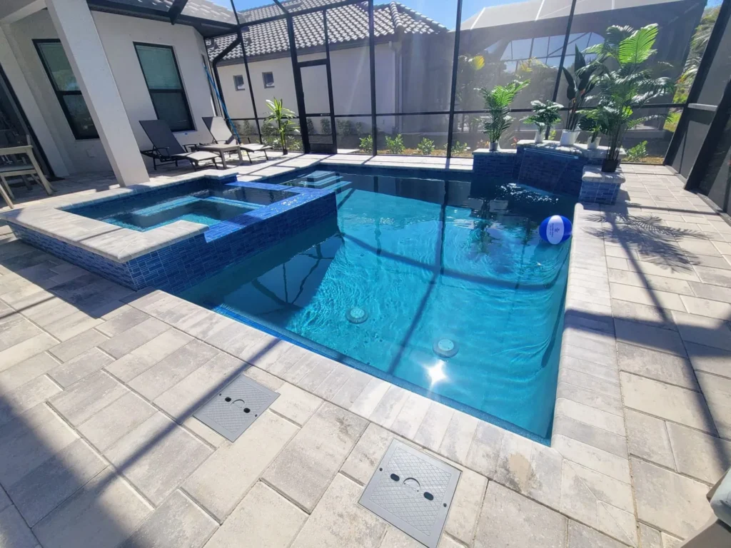 A rectangular pool with an attached spa and tiled water feature pedestals under a screened lanai.