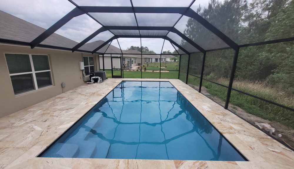 A rectangular pool with travertine deck under a full screen enclosure on an overcast day.