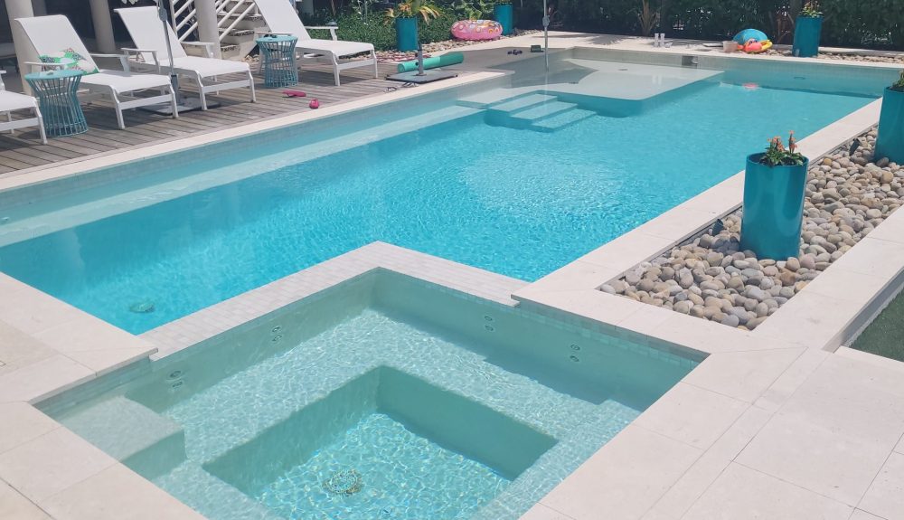 A rectangular pool with an attached raised spa, tanning ledge, and stone-and-wood decking under open sky.