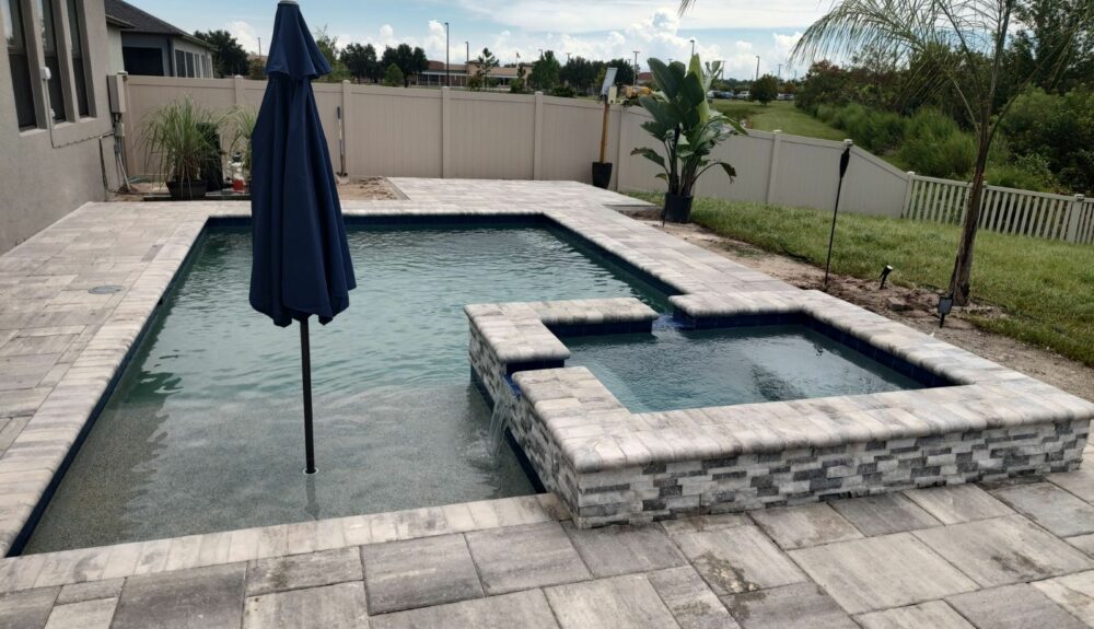 A rectangular backyard pool with a raised spa that spills water over a stacked-stone wall into the pool.